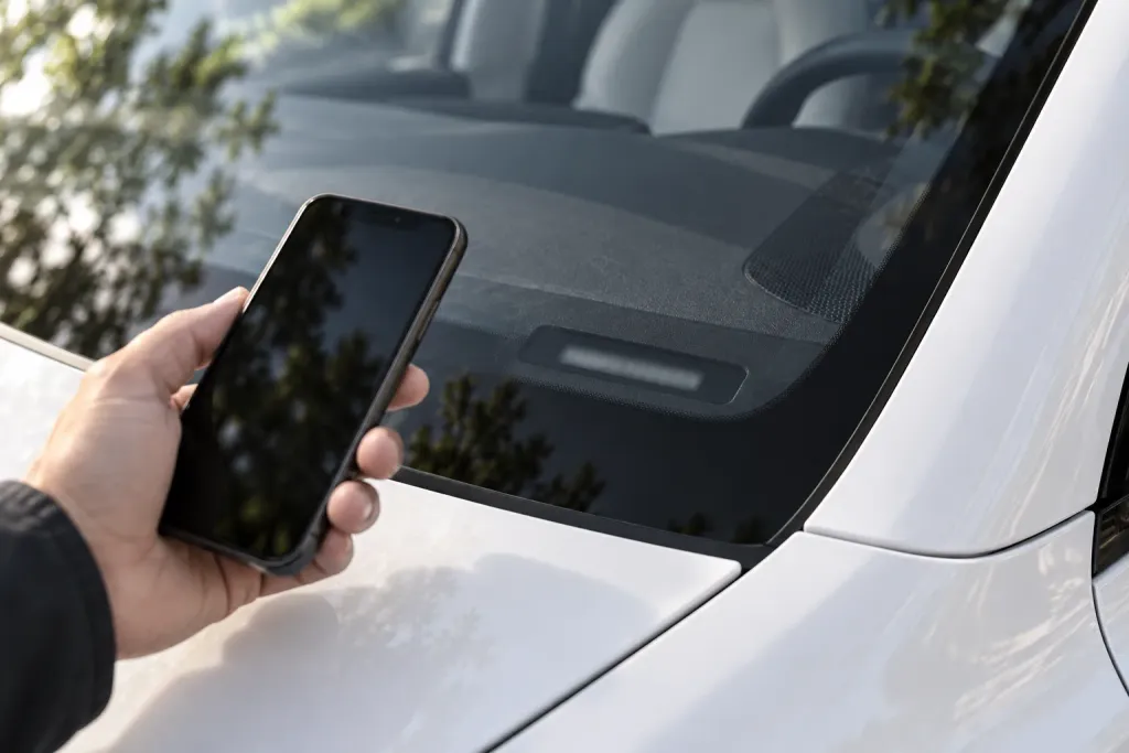 A hand holding a smartphone beside the windshield of a white Tesla, the dashboard plate out of focus (AI-generated image)